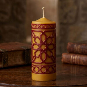 Bougie artisanale dorée avec motifs géométriques rouges sculptés, ambiance médiévale et décor ancienne.