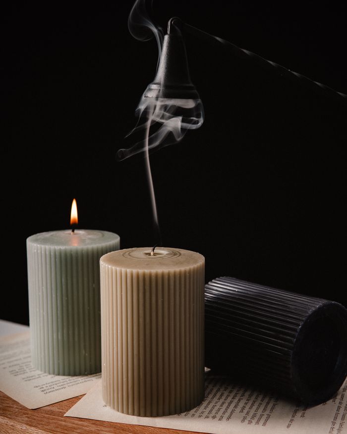 Three textured candles with smoke rising, captured in a dark studio setting.