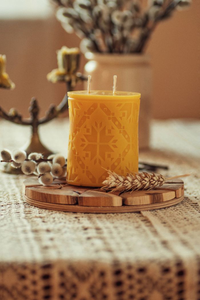 Yellow candle with intricate pattern on a rustic table with natural decor.