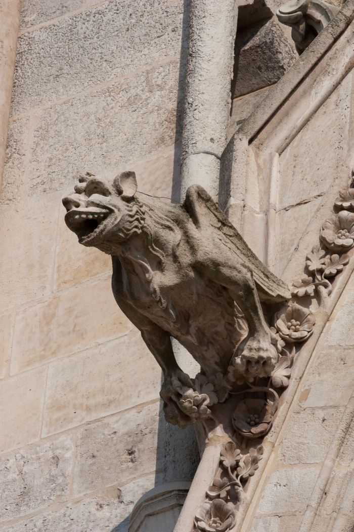 Close-up of a Gothic gargoyle statue carved on a stone cathedral wall under sunlight.